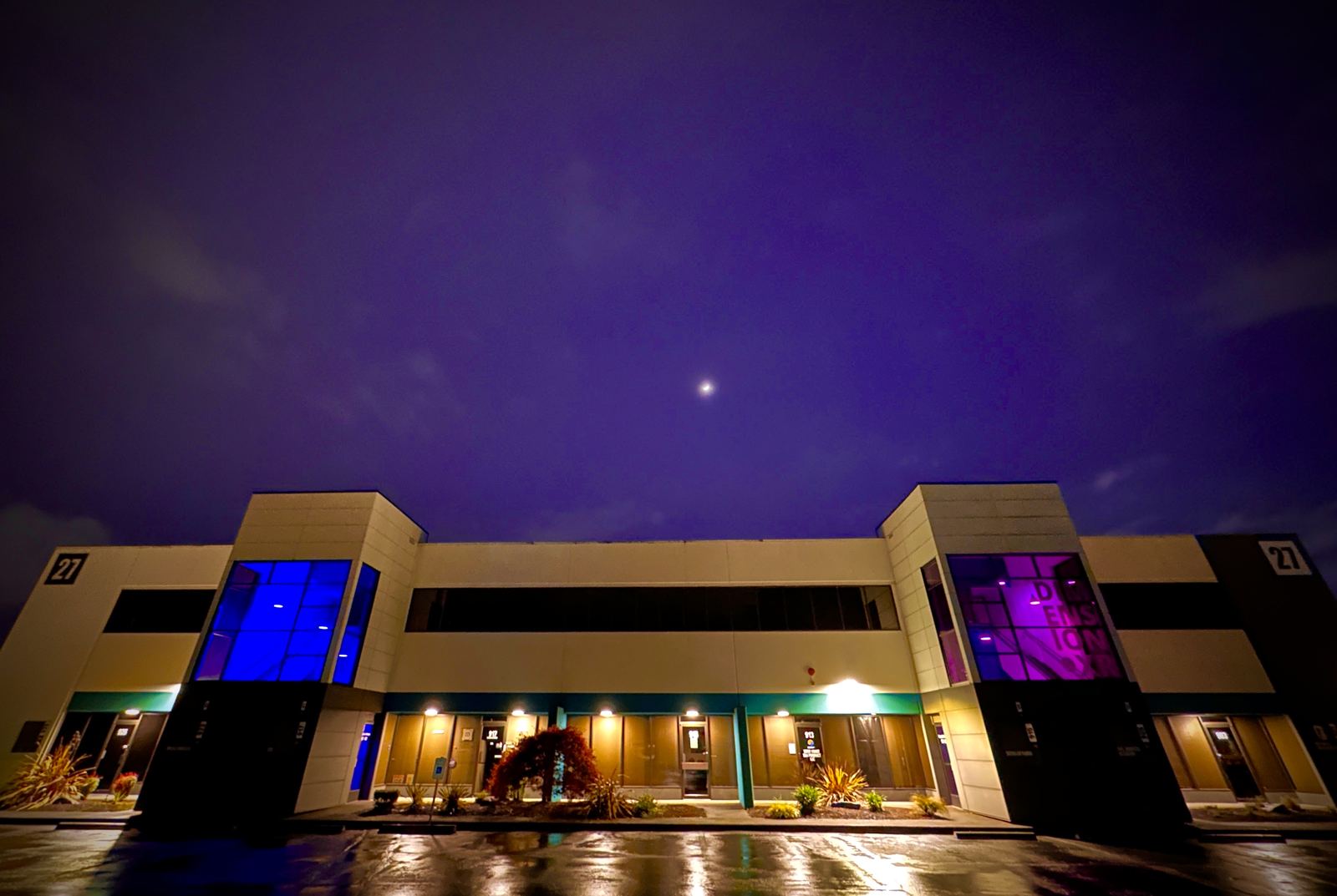 The Dimension XR building in Tukwila at night, its stairwell windows glowing blue and purple under a moonlit sky.